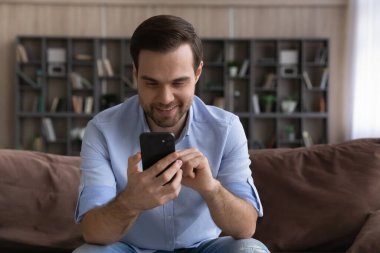 Gülümseyen milenyum erkeği koltukta oturur ve cep telefonuyla sohbet eder.