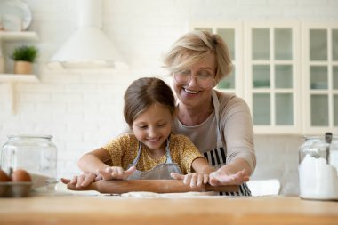 Mutlu yetişkin büyükanne küçük sevimli torununa hamuru yuvarlamayı öğretiyor.