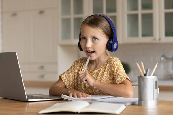 Grappig duur klein meisje in hoofdtelefoon studeren online thuis — Stockfoto