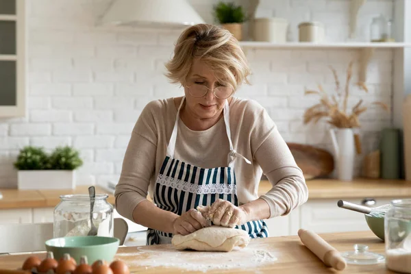 Mujer madura en vasos amasando masa en la cocina moderna —  Fotos de Stock