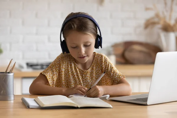 Close-up klein meisje in hoofdtelefoon het maken van notities studeren online — Stockfoto