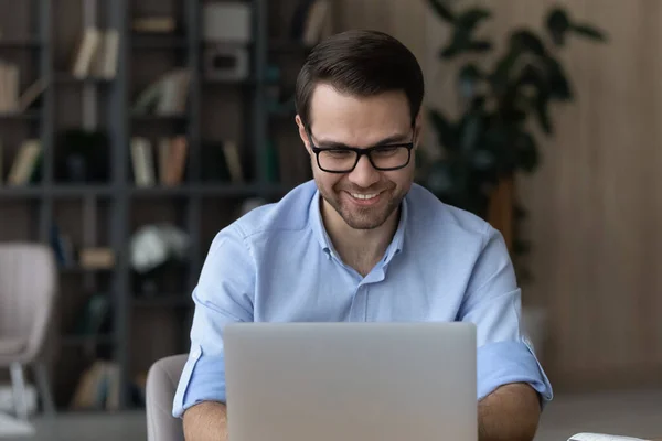 Gülümseyen genç erkek işçi masa başında bilgisayar tipi belge kullanıyor — Stok fotoğraf