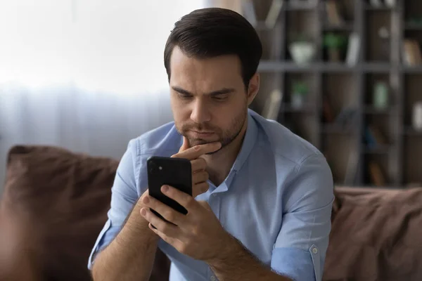 Thoughtful millennial man rubbing chin reading important phone message — Stock Photo, Image