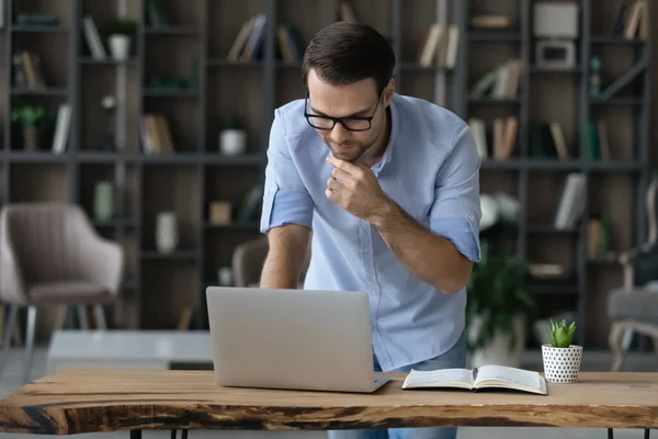 Focused young man stand by table look on laptop screen