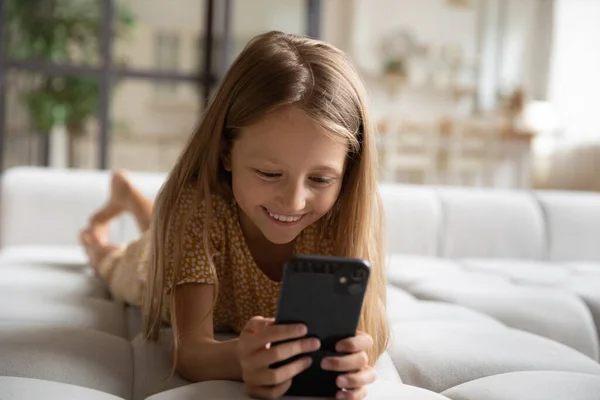 Close up smiling little girl using smartphone lying on couch — Stock Photo, Image