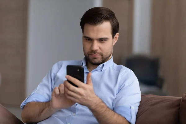 Focused guy spend time on couch browse web on phone — Stock Photo, Image