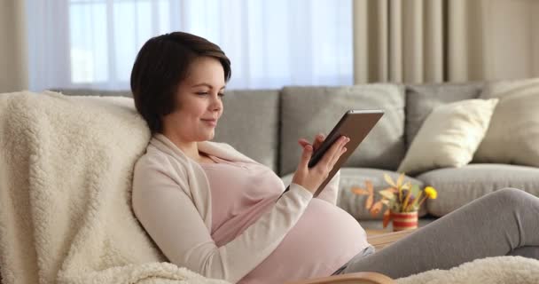 Uśmiechnięta, zrelaksowana kobieta w ciąży za pomocą tabletu cyfrowego. — Wideo stockowe