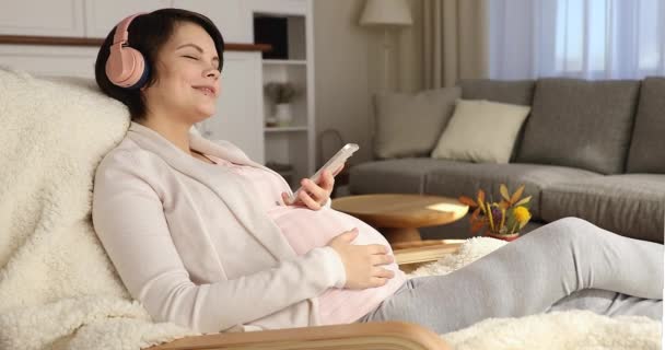 Ειρηνική νεαρή ευτυχισμένη έγκυος γυναίκα ακούγοντας μουσική στα ακουστικά. — Αρχείο Βίντεο