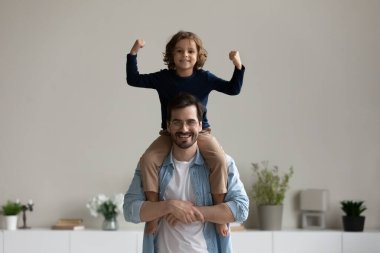 Heyecanlı çocuk babasının boynuna oturmuş, el hareketi yapıyor.