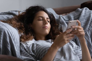 Tembel, umursamaz kadın yatakta dinleniyor, akıllı telefon kullanıyor.