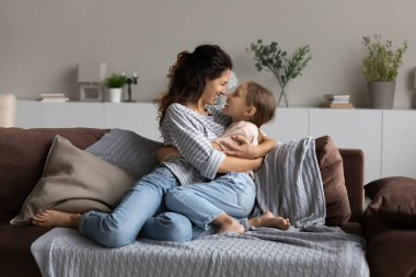Happy mom and little daughter girl hugging, resting on couch clipart