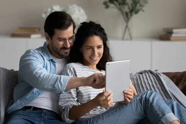 Happy relaxed millennial couple with tablet hugging on couch — Stock Photo, Image