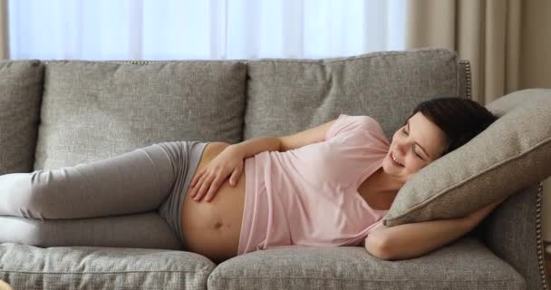 Heureuse belle jeune femme enceinte se détendre sur un canapé confortable. — Video