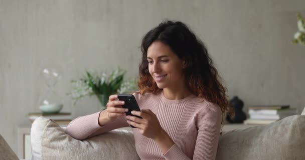 Entspannte junge lächelnde hispanische Frau nutzt Smartphone zu Hause. — Stockvideo