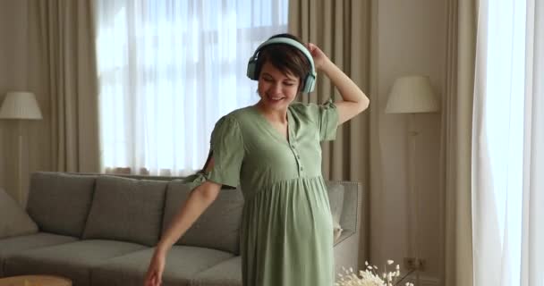Szczęśliwa młoda ciężarna kobieta tańczy, słucha muzyki w słuchawkach. — Wideo stockowe