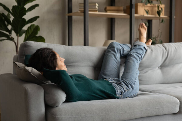 Закройте мирную босиком молодую женщину, отдыхающую на диване