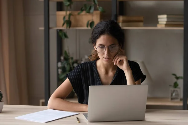 Закрыть вдумчивую деловую женщину в очках, глядя на экран ноутбука — стоковое фото