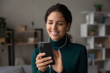 Kafasından vurulmuş, kulaklıklı, gülümseyen bir kadın akıllı telefon kullanıyor.