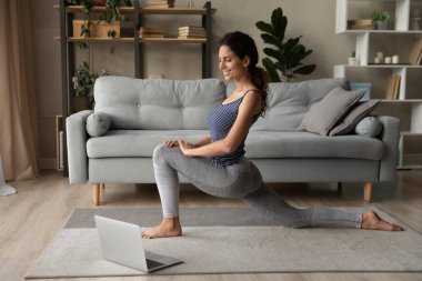 Gülümseyen kadın internetten yoga yapıyor, esniyor, dizüstü bilgisayara bakıyor.