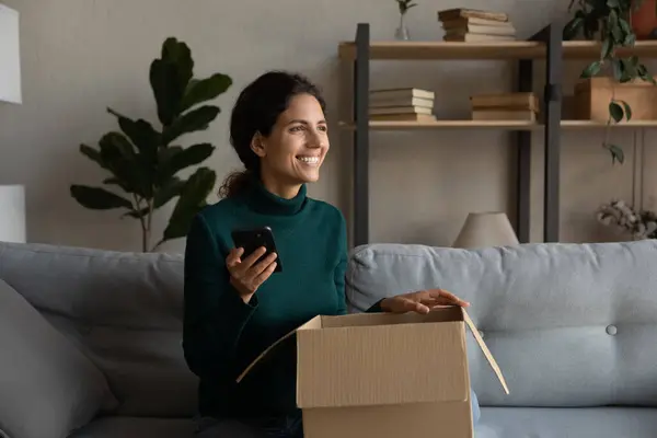 Mujer sonriente emocionada por el pedido en línea, sosteniendo el teléfono inteligente, caja de apertura —  Fotos de Stock