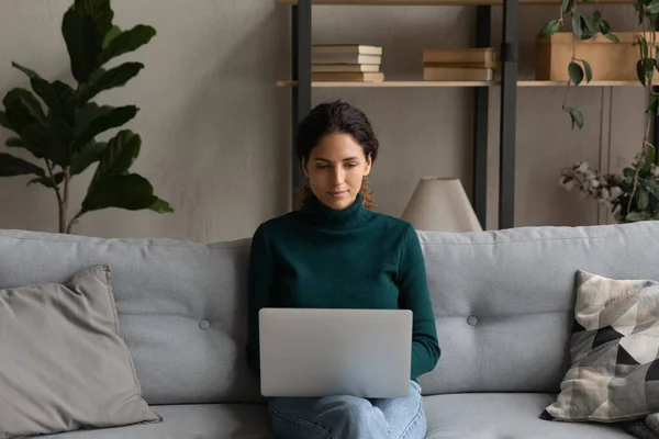 Confident young woman with laptop on laps sitting on couch