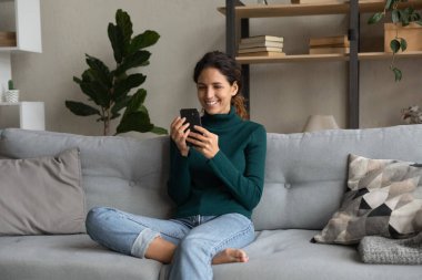 Akıllı telefonuyla koltukta dinlenen gülümseyen kadın, internet uygulamaları.
