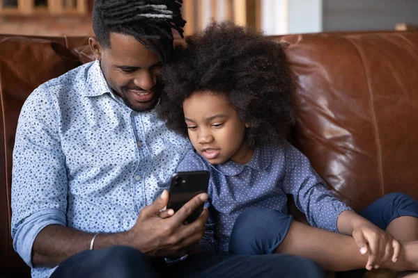 Happy African American dad and daughter use smartphone