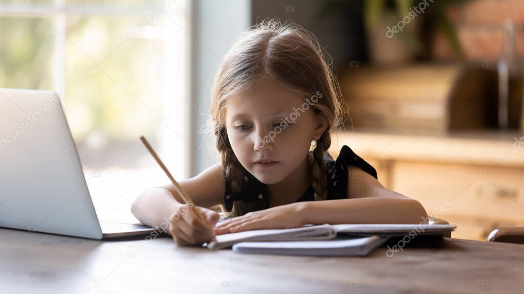 Focused gen Z little girl studying from home, writing notes