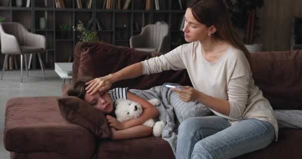Strachující mladá maminka kontroluje teplotu nemocné dcerušky. — Stock video