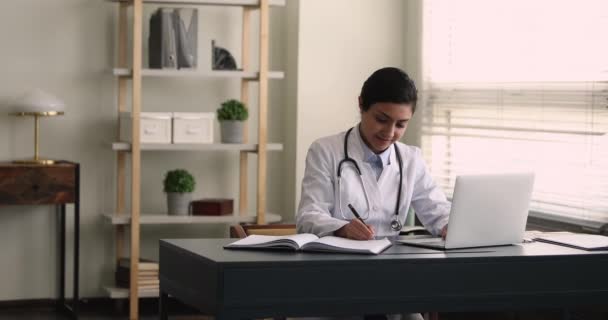 Médico indiano trabalhando em laptop escreve em jornal médico — Vídeo de Stock