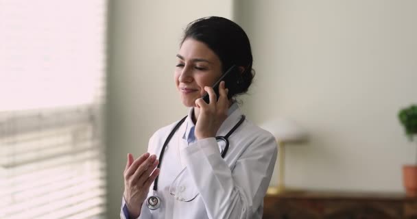 Индийский врач общей практики, стоящий на рабочем месте и разговаривающий по телефону — стоковое видео