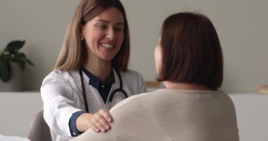 Gülümseyen genç bayan doktor yaşlı hastayı destekliyor..