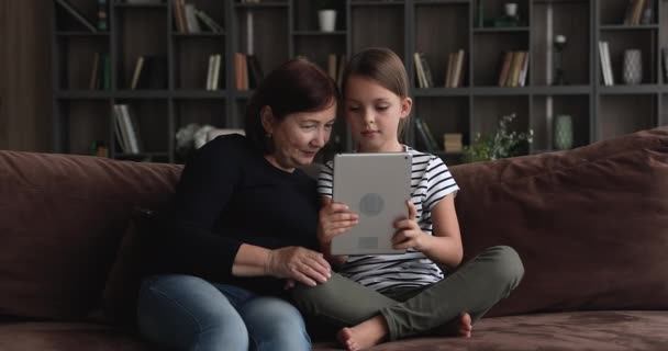 Умная маленькая девочка учит старую бабушку пользоваться планшетом. — стоковое видео