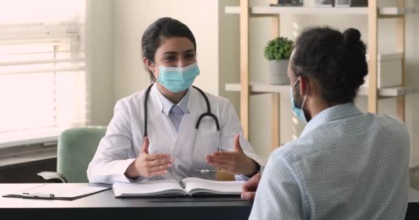 Médico indio usar mascarilla protectora de seguridad hablar con paciente africano — Vídeos de Stock