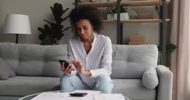 Focused happy african woman calculating expenditures using mobile app. — Stock Video