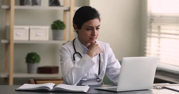 Young Indian general practitioner working on laptop in clinic office — Stock Video