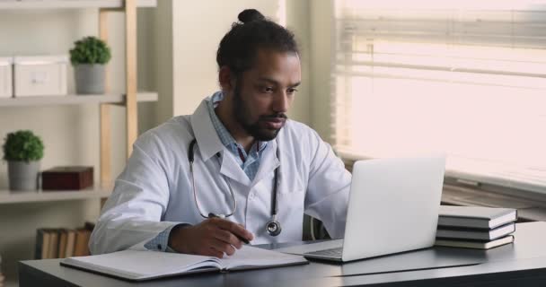 Afrikanischer Arzt schreibt Patientenanamnese in Tagebuch, surft im Internet — Stockvideo