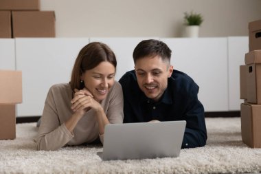 Çift, dizüstü bilgisayarla halının üzerinde yatıp ev eşyaları alıyor.