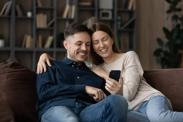 Happy couple sit on sofa use smartphone enjoy new application — Photo