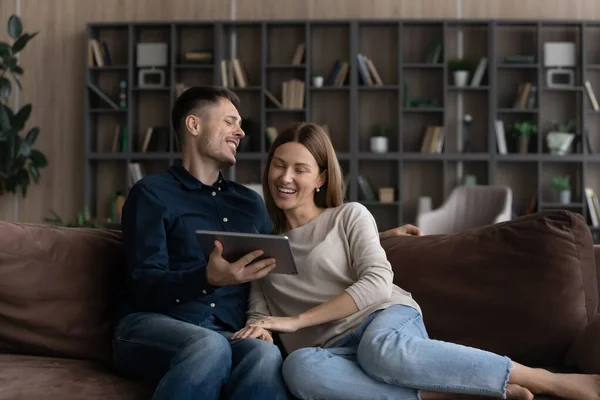 Laughing couple relaxing on sofa watch funny content on tablet — Stockfoto