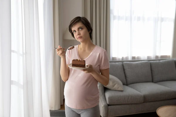 Thoughtful young pregnant woman eating dessert, holding plate with cake — Fotografia de Stock