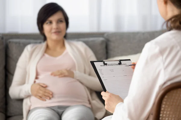 Doctor filling medical form at appointment with pregnant patient — Stock Photo, Image