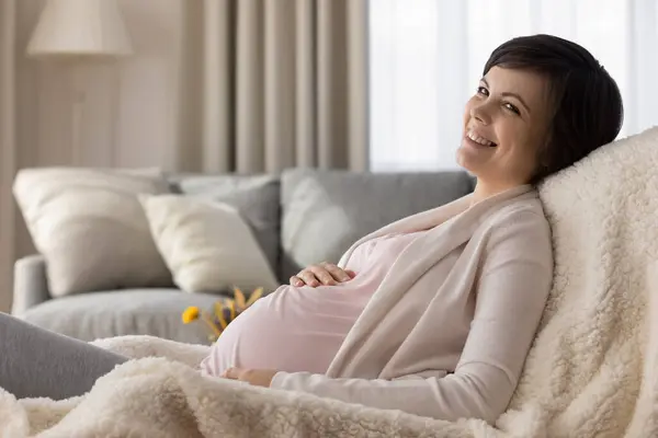 Lycklig gravid ung kvinna vilar i fåtölj hemma — Stockfoto