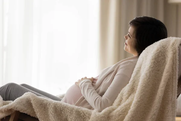 Happy dreamy expectant mother resting in armchair with soft blanket —  Fotos de Stock