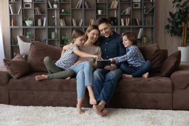Küçük çocuklu mutlu bir aile kanepede oturup tablet kullanır.