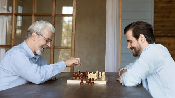 Smiling mature dad play chess with adult son — Stock Photo, Image