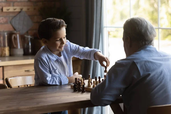 Smart little grandson play chess with old grandfather — стоковое фото