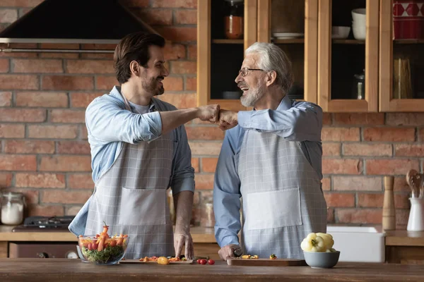 Smiling adult son and old dad cooking food — стоковое фото