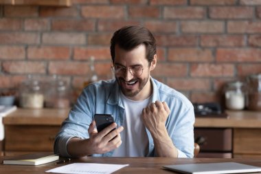 Excited millennial man triumph with good news on cell