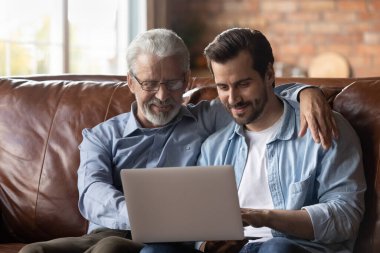 Happy adult son and old father use laptop at home